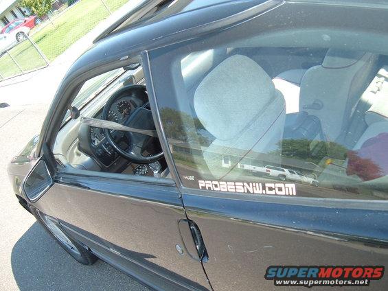 side view of black coupe interior, steering wheel, seats, and a "PROBESNW.COM" sticker on the window