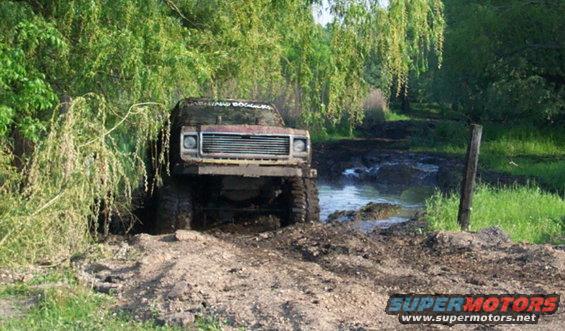 Mud-covered off-road vehicle with large tires driving through a muddy track and water. Text on windshield reads 'BARNYARD BOGGERS'