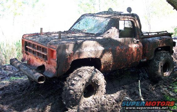 Mud-covered 1979 pickup truck stuck in deep mud, with large tires and a custom pipe bumper