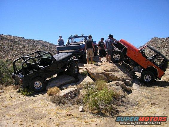 Three off-road vehicles, two Jeeps and a pickup truck, navigating rocky terrain under a clear blue sky