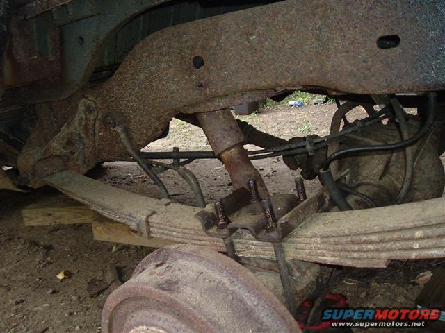 Rear axle and leaf spring suspension of a vehicle, showing rust and wear. Part of a Supermotors.net watermark is visible