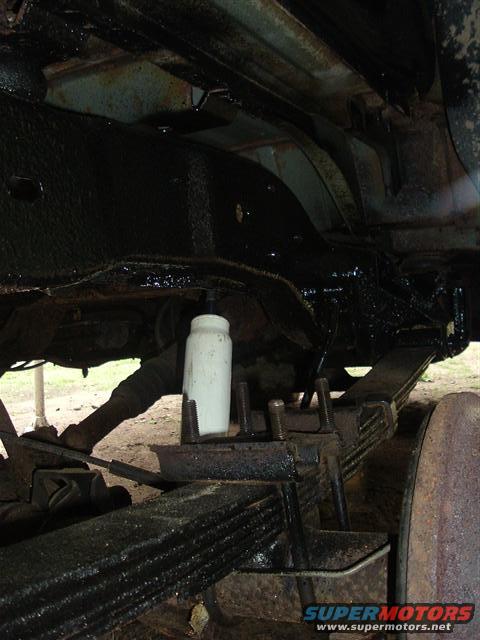 Undercarriage of a vehicle with black undercoating, showing leaf springs and a white shock absorber