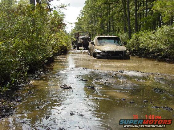 Muddy 1995 Dodge 1500 stuck in water, front view. Another truck behind