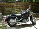 2004 Honda Shadow Sabre VT 1100 - A black cruiser motorcycle is parked outdoors on a paved surface, with a wooden fence in the background.