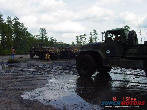 Military trucks in muddy terrain with two people standing nearby