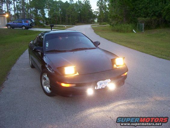 Black coupe with pop-up headlights on a road. License plate says MY TOY