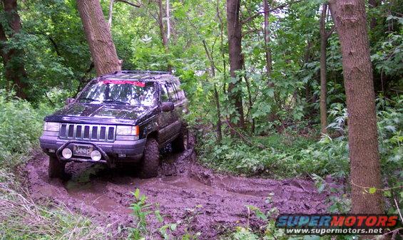 Black Jeep Grand Cherokee navigating a muddy trail with trees surrounding