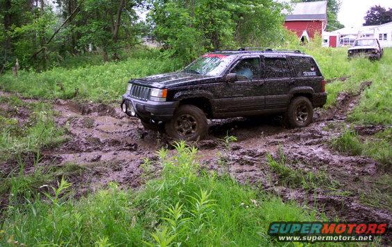 Black Jeep Grand Cherokee stuck in mud on a trail, another vehicle visible in background