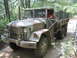 1990 Ford Bronco - This military truck is driving on a dirt road through a forest. The vehicle has a camouflage paint scheme.