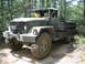 1990 Ford Bronco - A military truck with a flatbed is driven off-road through a wooded area.