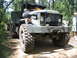 1990 Ford Bronco - A large, olive-drab military truck with a prominent grille is shown on a wooded dirt path.