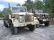 1990 Ford Bronco - Two military trucks are parked on a dirt road with trees in the background.