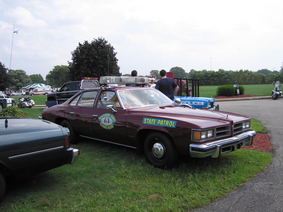 Maroon police car with light bar and "STATE PATROL" text, parked on grass