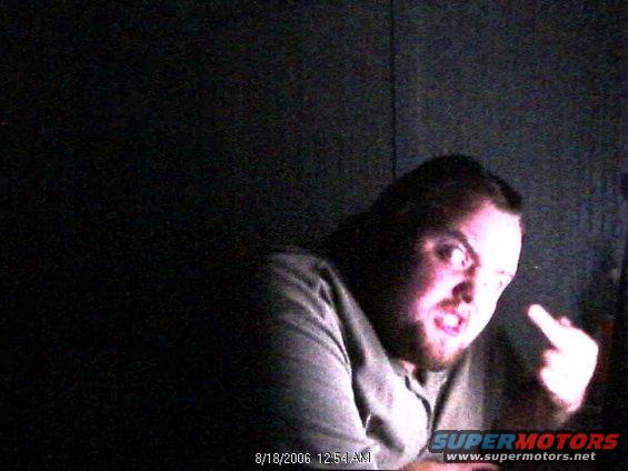 Man with beard and angry expression, giving the middle finger, with a timestamp and website overlay