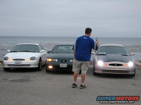 Three Ford Taurus sedans parked by the ocean, one with a black hood