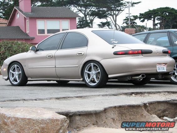 tan sedan parked on street, another car next to it, pink house in background