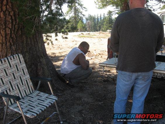 Two guys hanging out by a tree with a chair and a truck bed visible