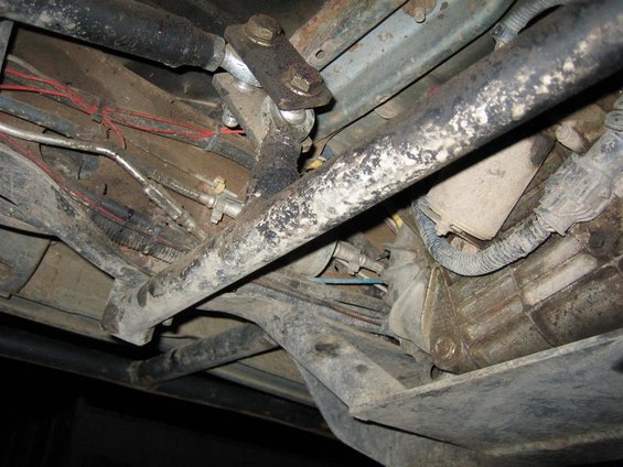 Undercarriage of a vehicle with visible suspension components, brake lines, and transmission housing