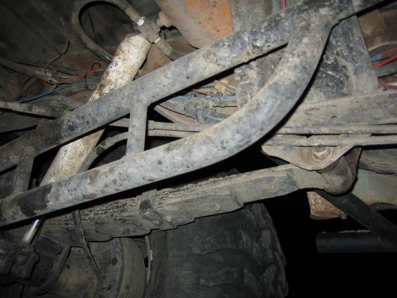 Underside of a vehicle showing suspension, leaf springs, and a tire. Lots of metal bars and wiring are visible