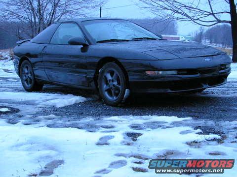 Black 1993 Ford Probe parked on a snowy surface with bare trees in the background