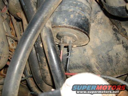 Engine compartment with black hoses and a black cylindrical component with wires. Text overlay reads SUPERMOTORS