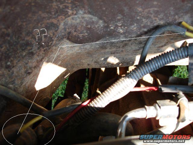 Undercarriage of a vehicle with rusted metal, corrugated tubing, and yellow and red wires. A white circle highlights some wiring