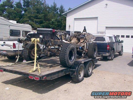 Chassis and drivetrain on trailer, with pickup truck and RV in background