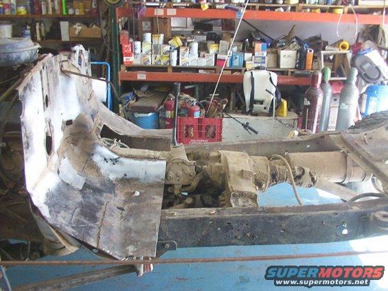 Rusty vehicle chassis with transmission and transfer case visible, in a workshop