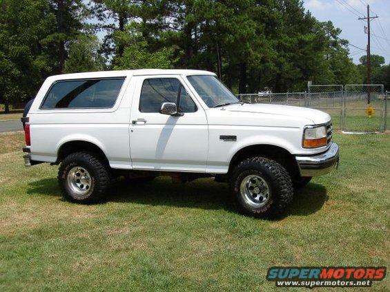 White Ford Bronco parked on grass, side view. It has aftermarket wheels and tires