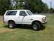 1993 Ford Bronco - This white Ford Bronco is shown from the front three-quarter view, parked on a grassy area with trees in the background.