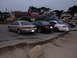1995 Ford Taurus - A row of sedans and a minivan are parked near the coast, with houses in the background.