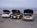 1995 Ford Taurus - Three Ford Tauruses are parked in front of the ocean with their hoods open.