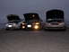 1995 Ford Taurus - Three Ford Taurus cars are parked in a row with their hoods open, illuminated by their headlights against the twilight sky.