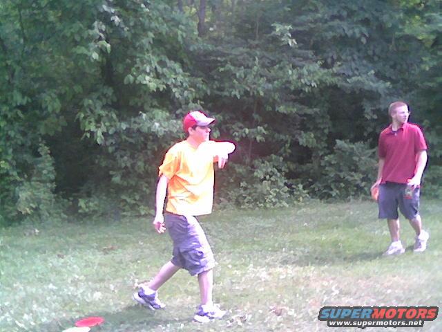 Two men playing disc golf in a grassy, wooded area