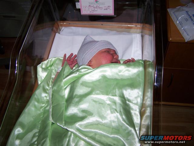 Baby in a hospital bassinet wearing a hat and wrapped in a green blanket