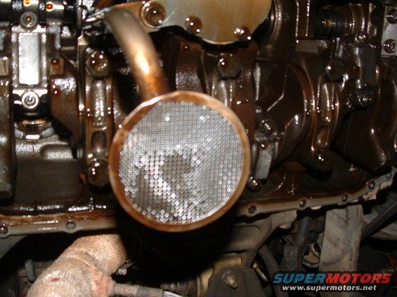 Engine oil pump pickup screen with mesh filter, partially obscured by engine components