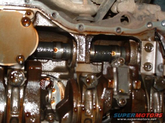 Engine crankshaft and camshafts with oil residue. Watermark reads SUPERMOTORS.NET