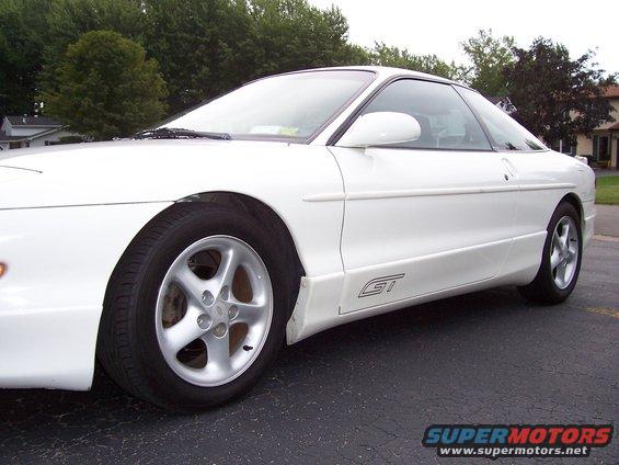 White coupe with GT badge on the lower body panel. Five-spoke wheels visible