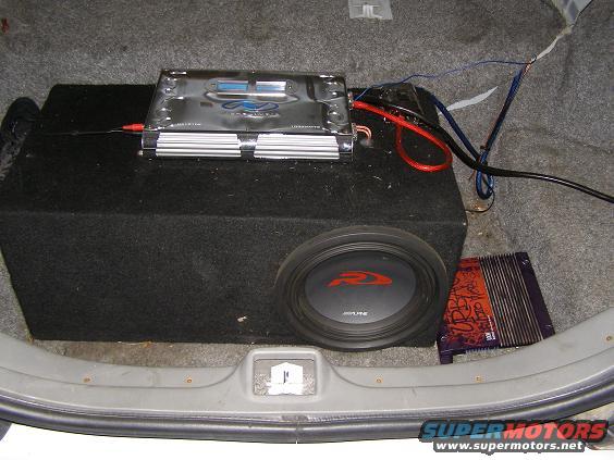 Car trunk interior with a large subwoofer box, amplifier, and wiring