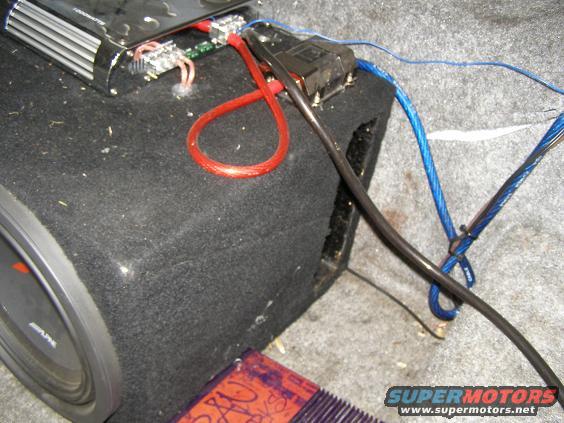Car audio amplifier connected to a subwoofer with red and blue wiring. A fuse holder is visible