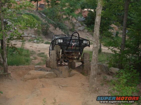 Black off-road vehicle with a roll cage, front tires on rocks, on a dirt trail