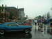 1978 Ford Mustang II - A blue coupe is parked on a wet street during an outdoor event with many people holding umbrellas.