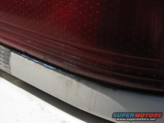 Close-up of a red taillight assembly with a chrome trim piece below it. The trim shows signs of wear and peeling