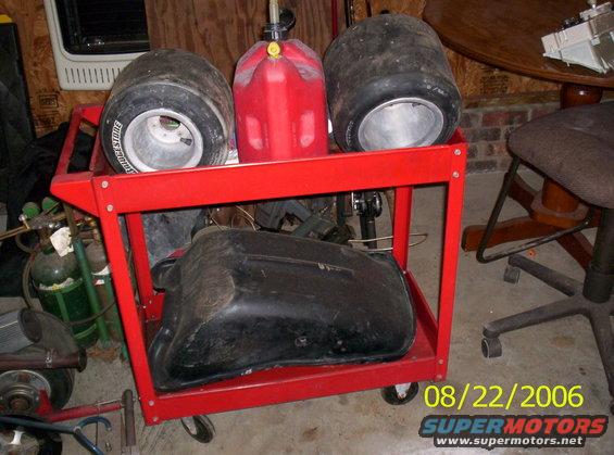 Red cart holding two racing tires, a red gas can, and a black fuel tank. Date stamp 08/22/2006