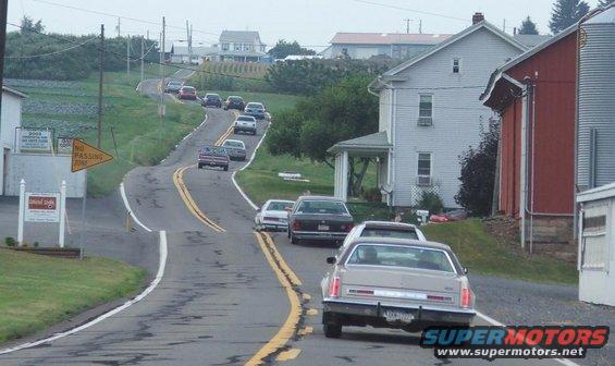 cars driving on a winding country road past houses and farms