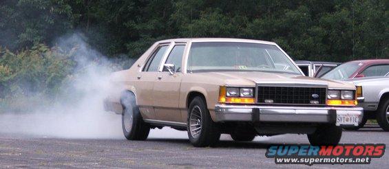 Tan 1985 Ford Crown Victoria LTD doing a burnout, front 3/4 view