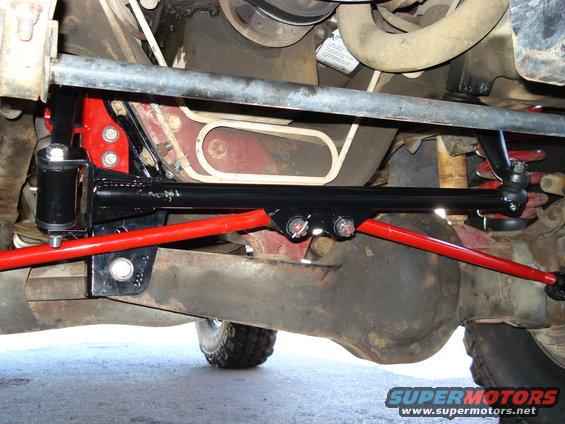 Undercarriage view of red and black suspension parts, including a sway bar and linkage, attached to a vehicle's differential and frame