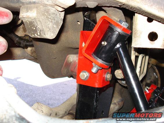 Close-up of a red and black aftermarket suspension part bolted to a vehicle's undercarriage