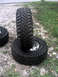 1996 Ford Bronco - Two large, aggressive off-road tires are stacked on a gravel surface next to grass.