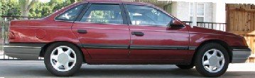 maroon sedan parked outdoors, side view. Body style suggests early 1990s